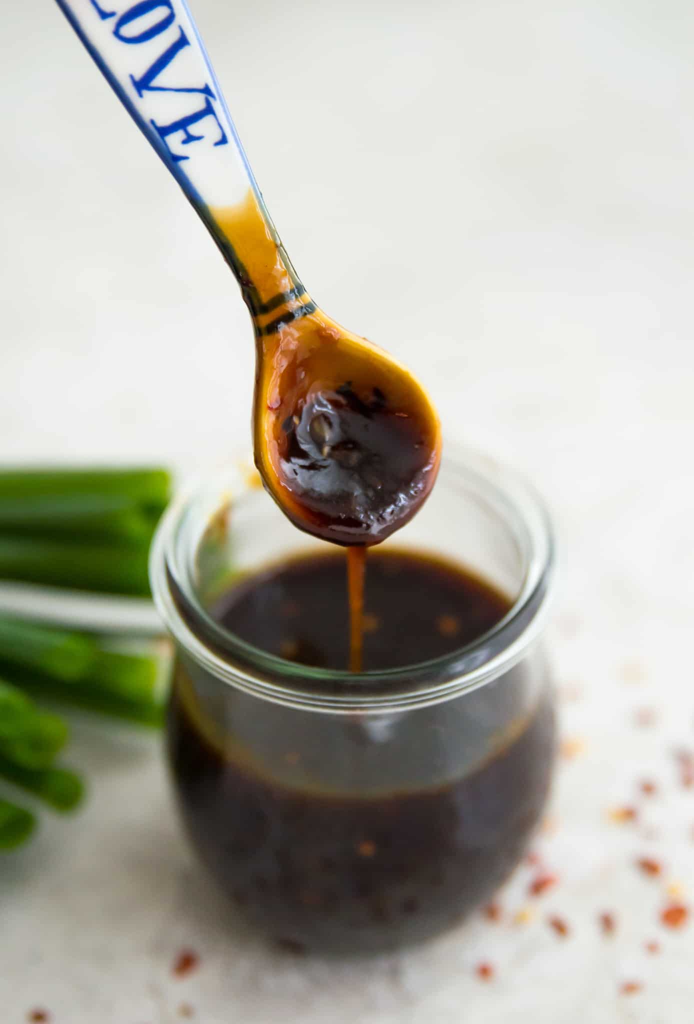 A spoon being dipped into a jar of teriyaki sauce. 