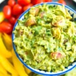 a bowl filled with a chunky guacamole with visible chunks of tomato and cilantro.