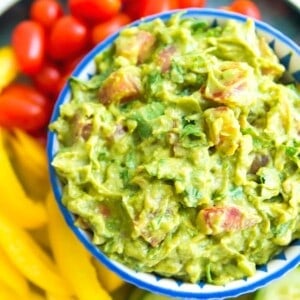 a bowl filled with a chunky guacamole with visible chunks of tomato and cilantro.