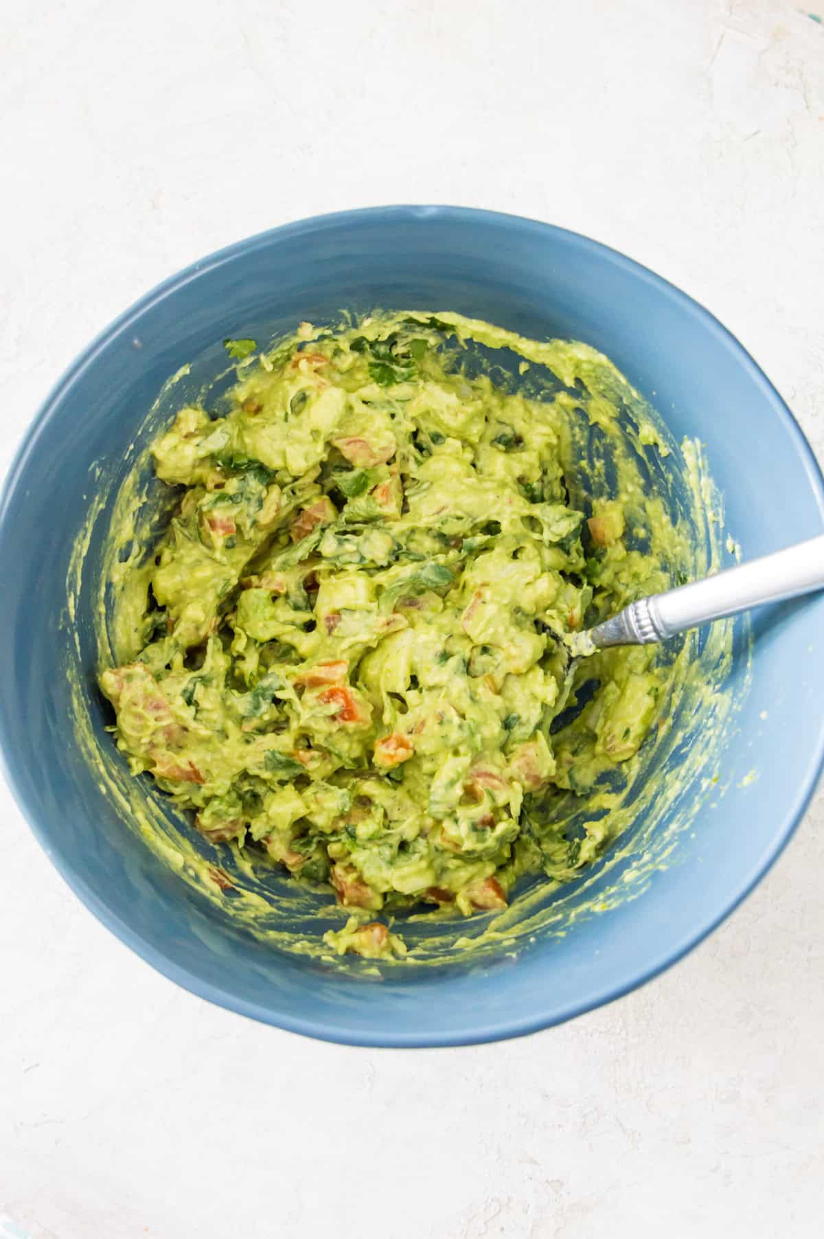 A bowl with pureed avocado in it with chunks of tomato and cilantro in the avocado.