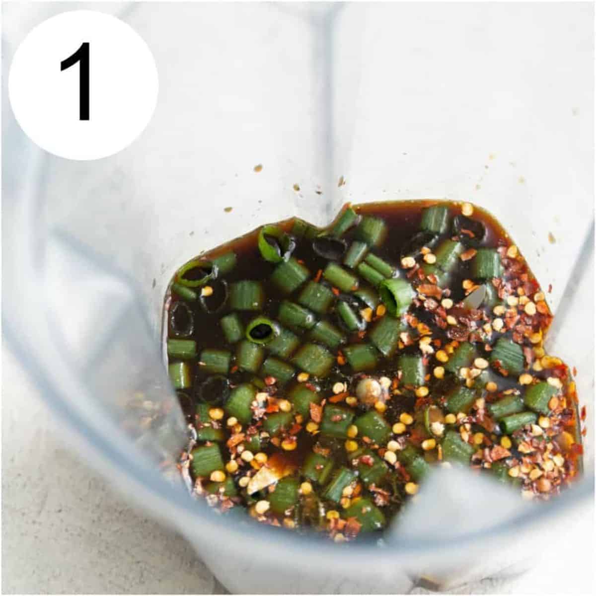 A blender with coconut aminos, chopped green onion and spices in it.