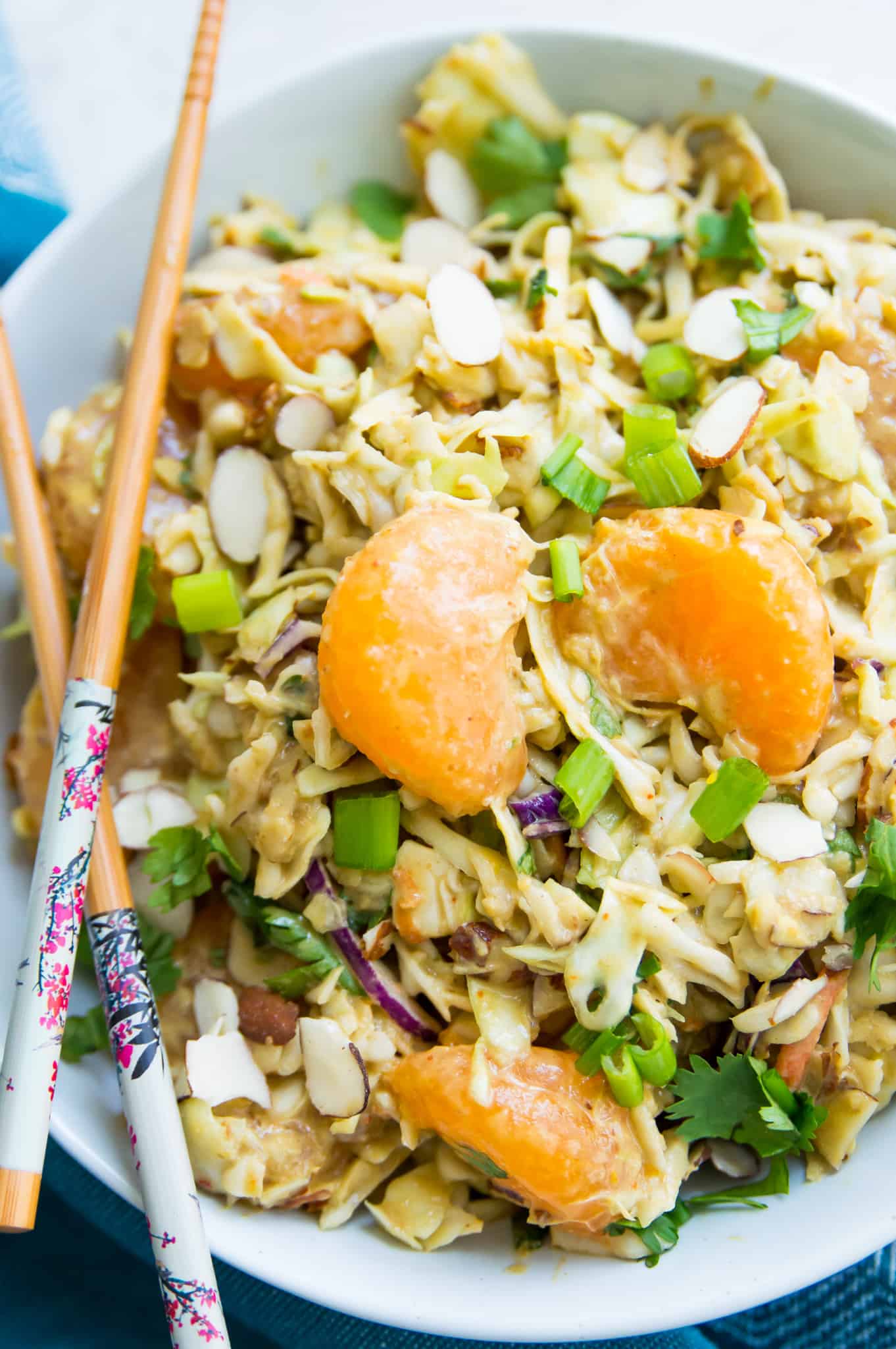 A bowl of asian coleslaw topped with mandarine oranges with chopsticks in the bowl. 