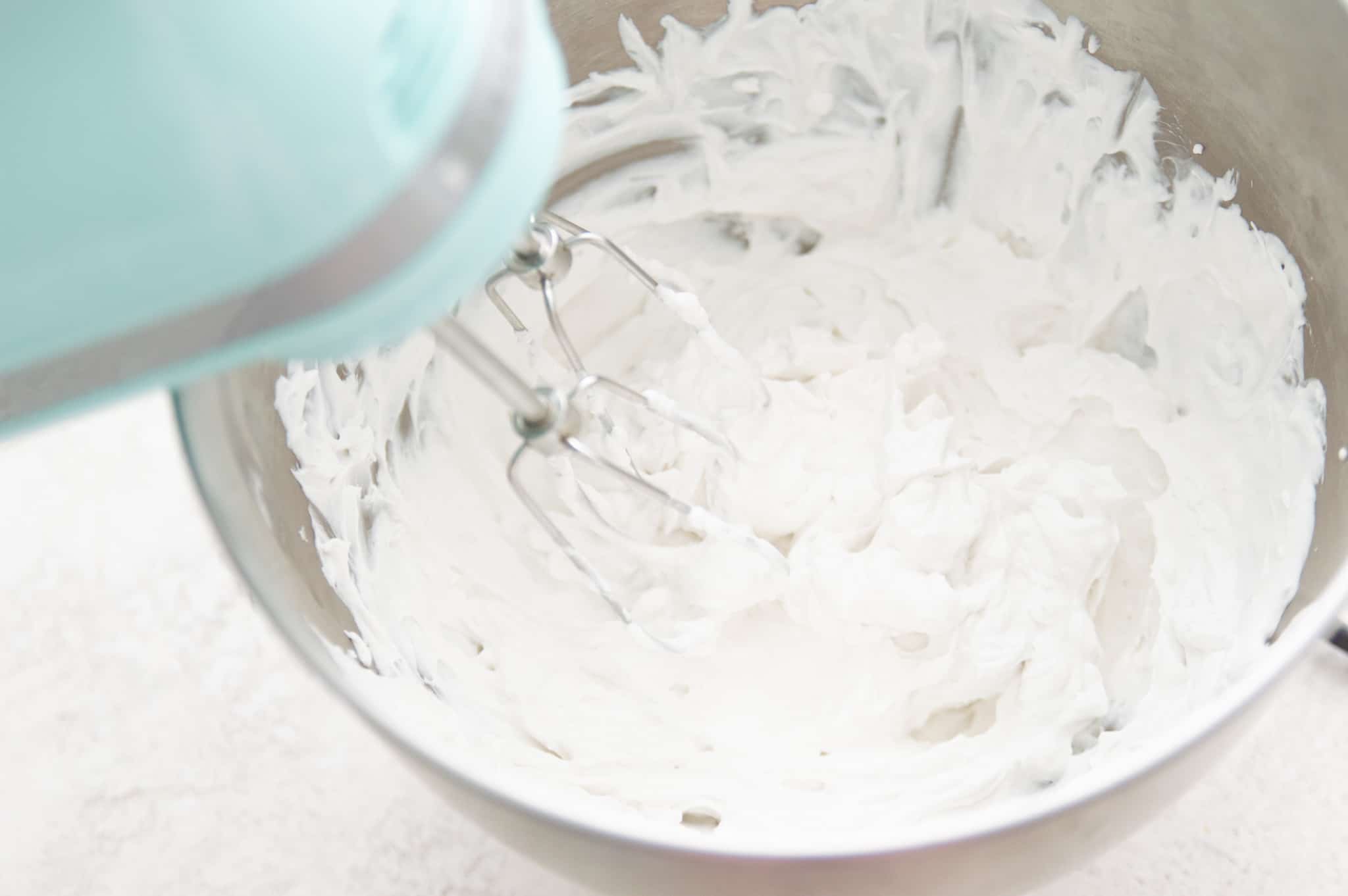 A hand mixer blending coconut cream in a bowl.