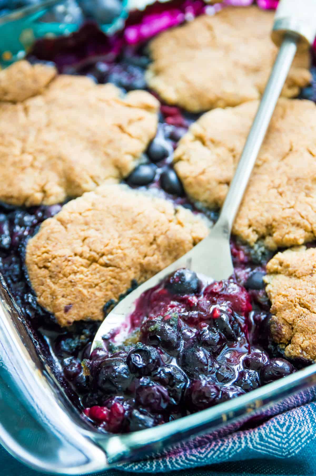 A pan of blueberry raspberry cobbler with a serving spoon in it.