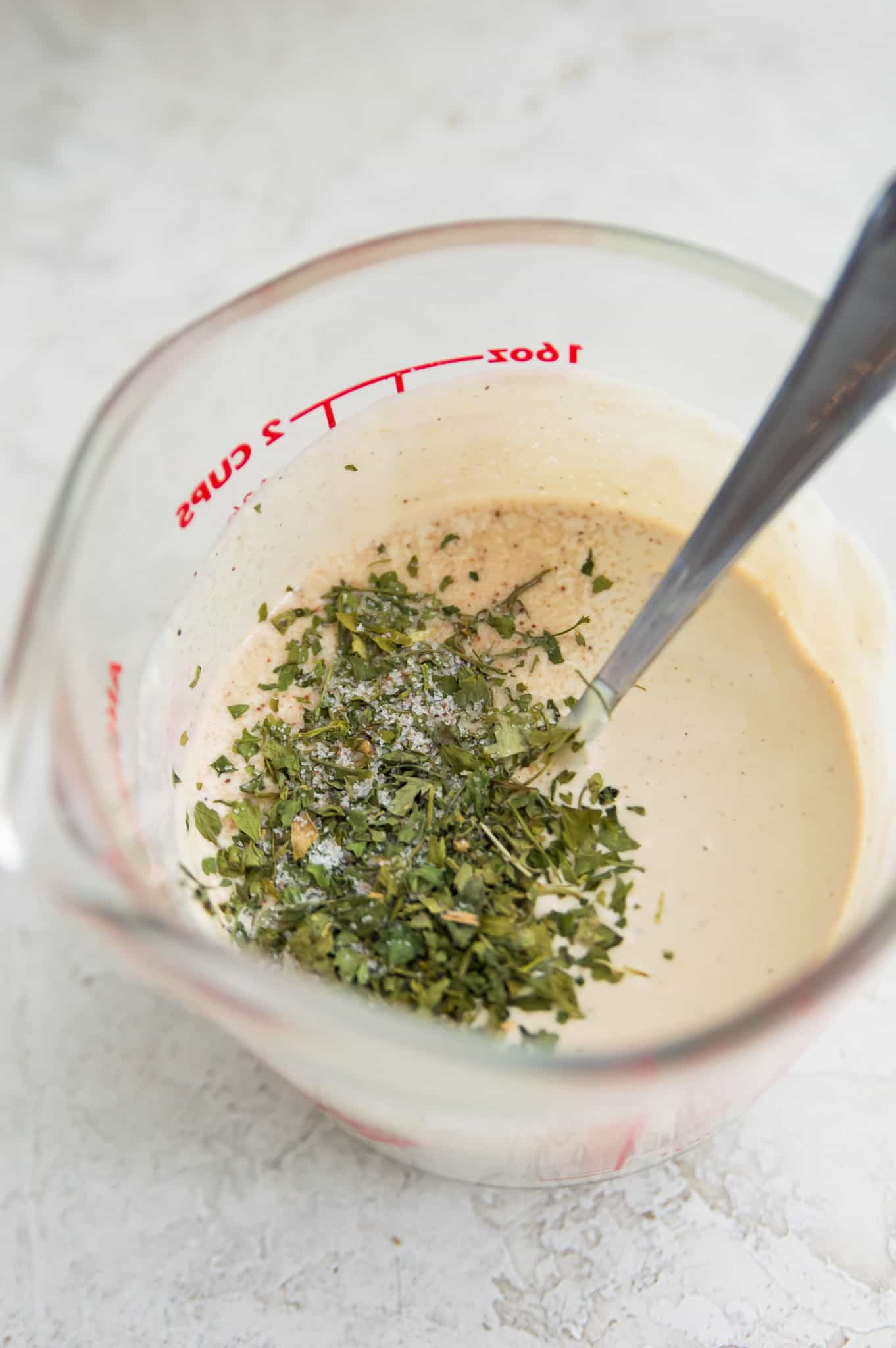 A glass measuring cup with a creamy dressing in it topped with dried basil.