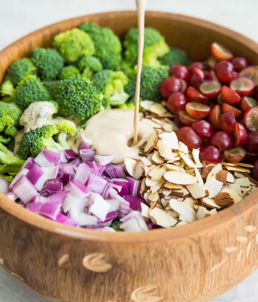 A bowl of broccoli salad with dressing being poured on it