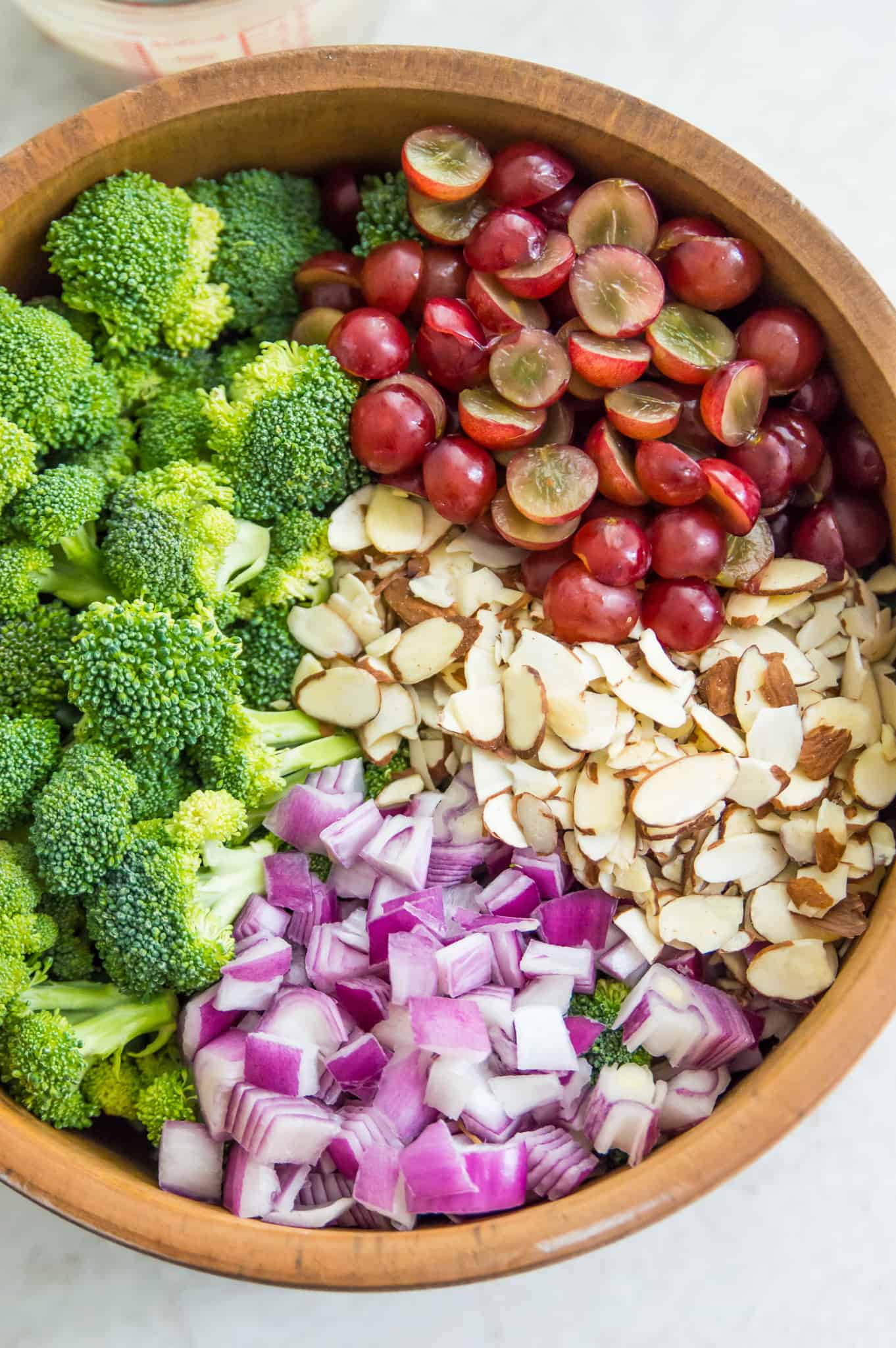 A large wooden bowl with chopped broccoli, grapes, red onion and slivered almonds in it.