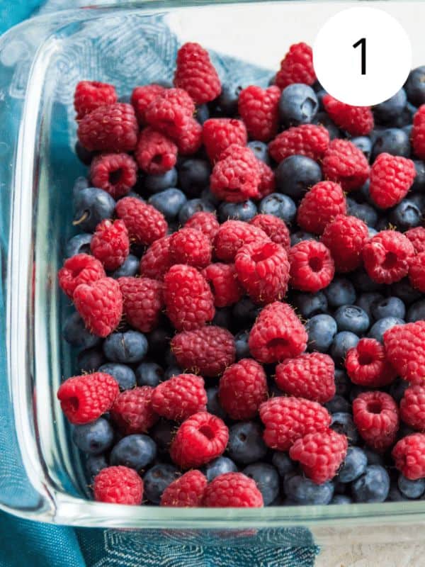 A glass baking dish with blueberries and raspberries in it.