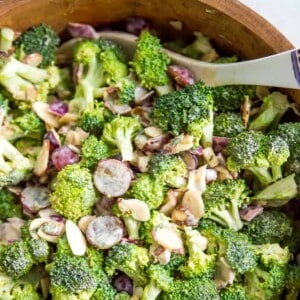 A bowl of healthy broccoli salad with a serving spoon in it.