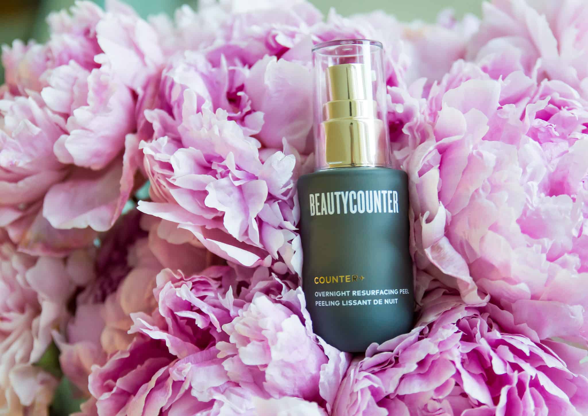 A bottle of the Beautycounter Overnight Resurfacing Peel in a bunch of pink peonies. 