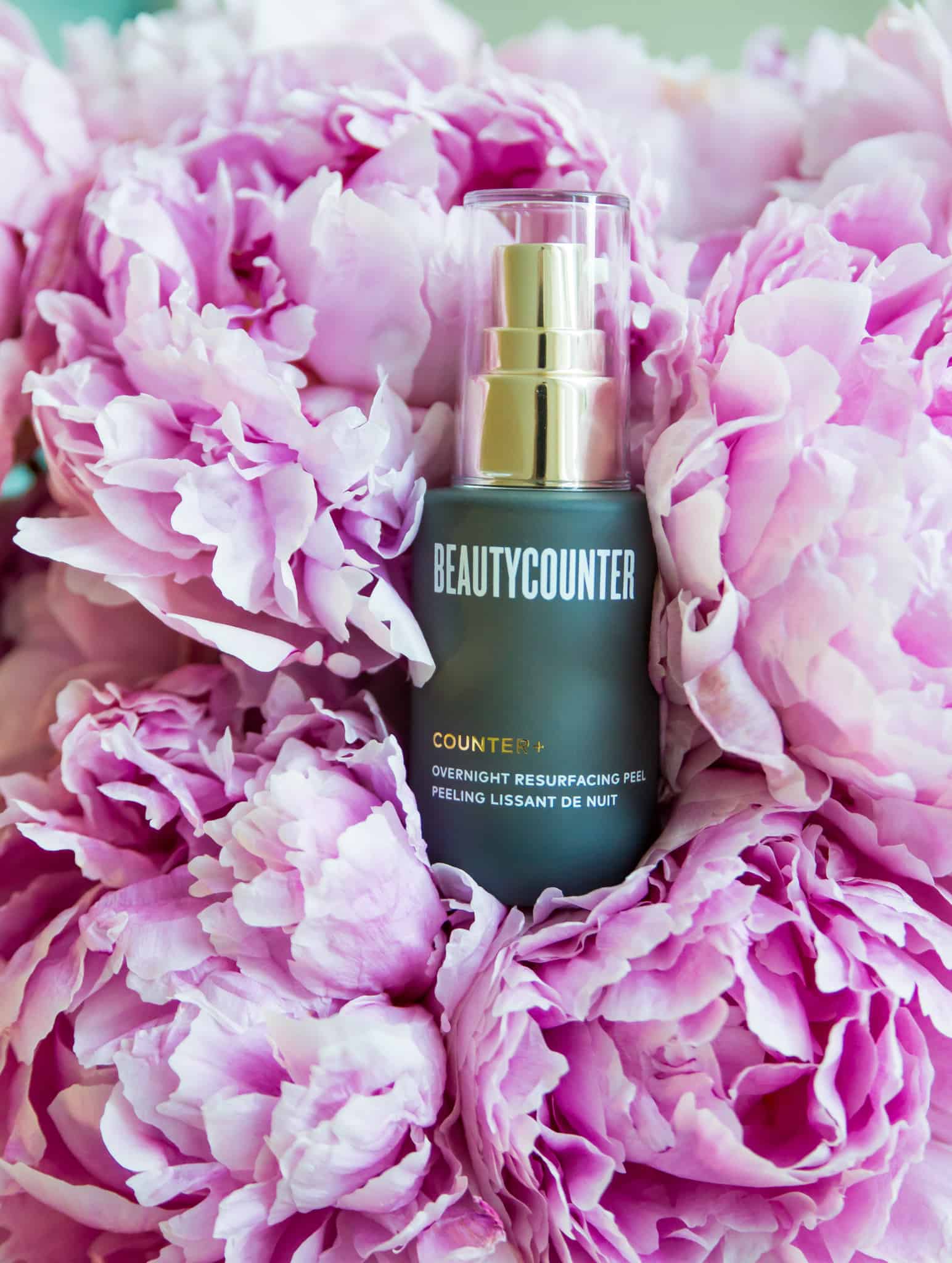 A bottle of Beautycounter's Overnight Resurfacing Peel in a bunch of pink peonies. 