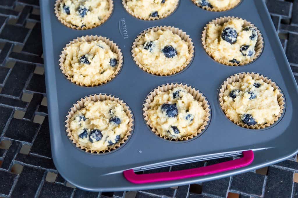 A muffin tray filled with the batter for making paleo lemon blueberry muffins.