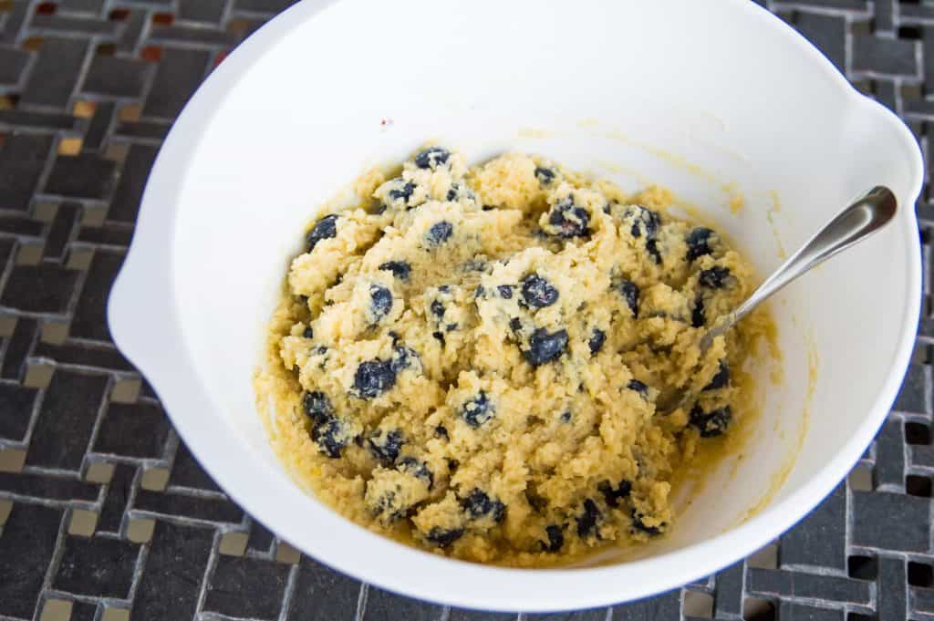 The batter for making paleo lemon blueberry muffins in a large bowl with a spoon in it.