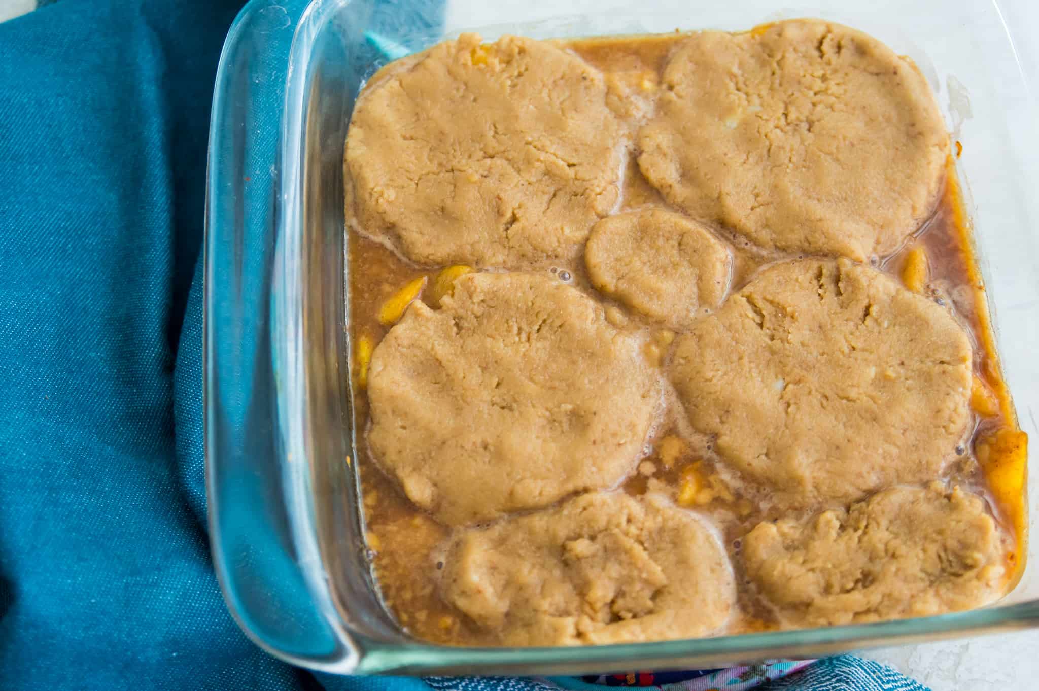 A baking dish with cooked peaches in it with dough on top of the peaches.