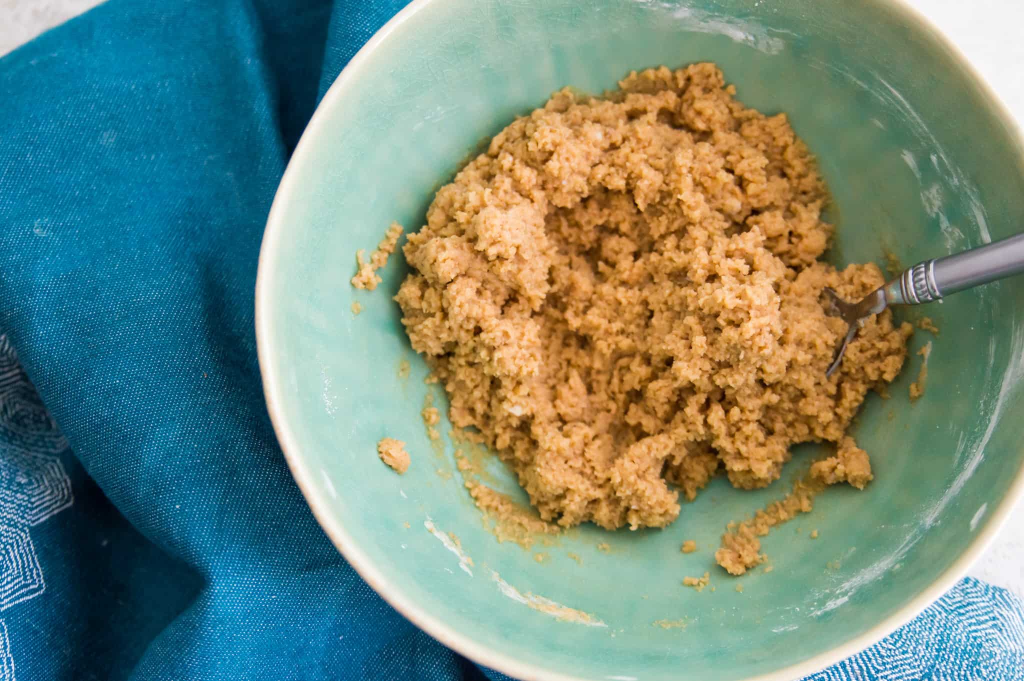 A bowl with dough in it and a spoon in the dough.