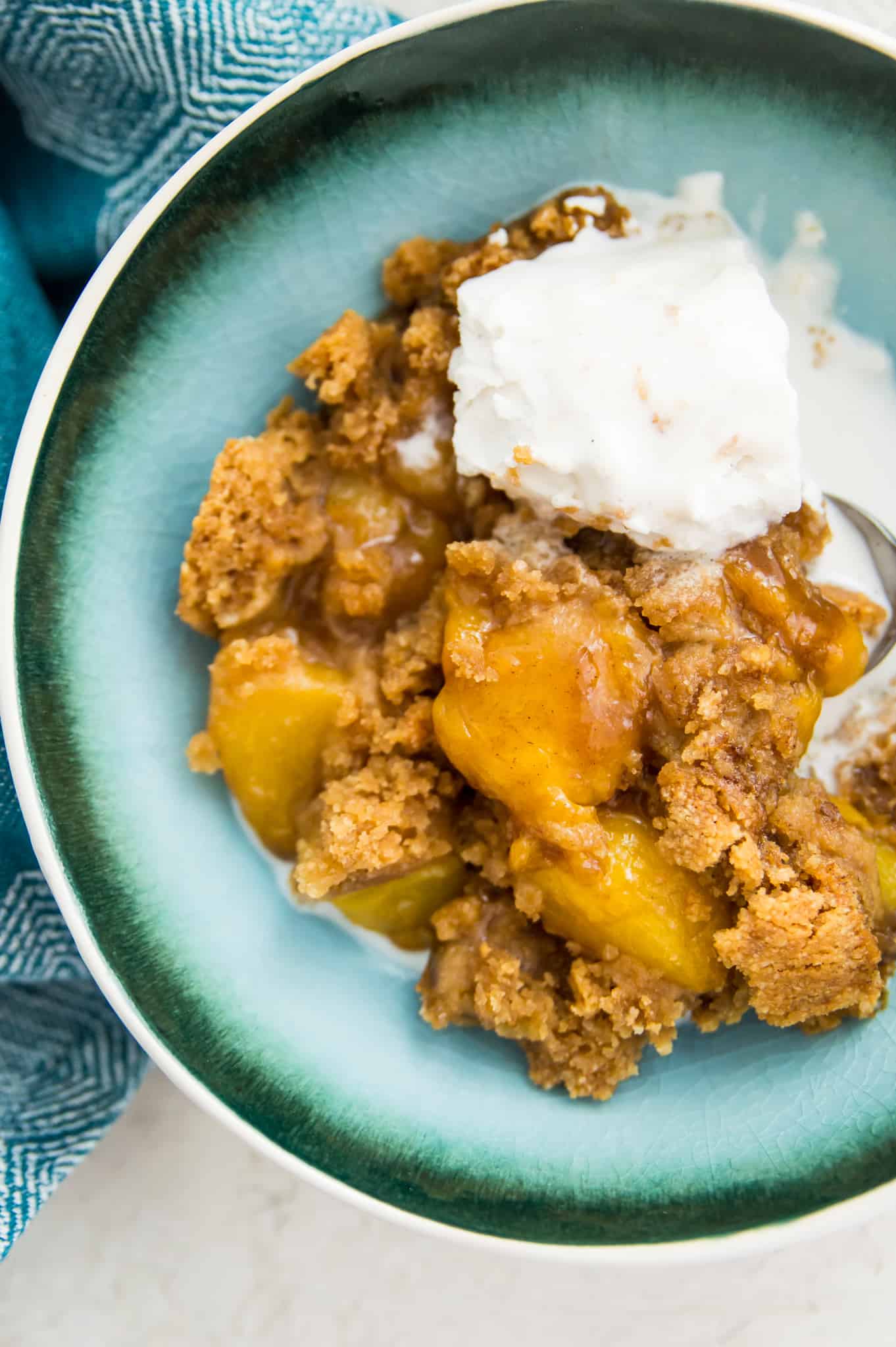 A bowl of peach cobbler with a scoop of vanilla ice cream on top.