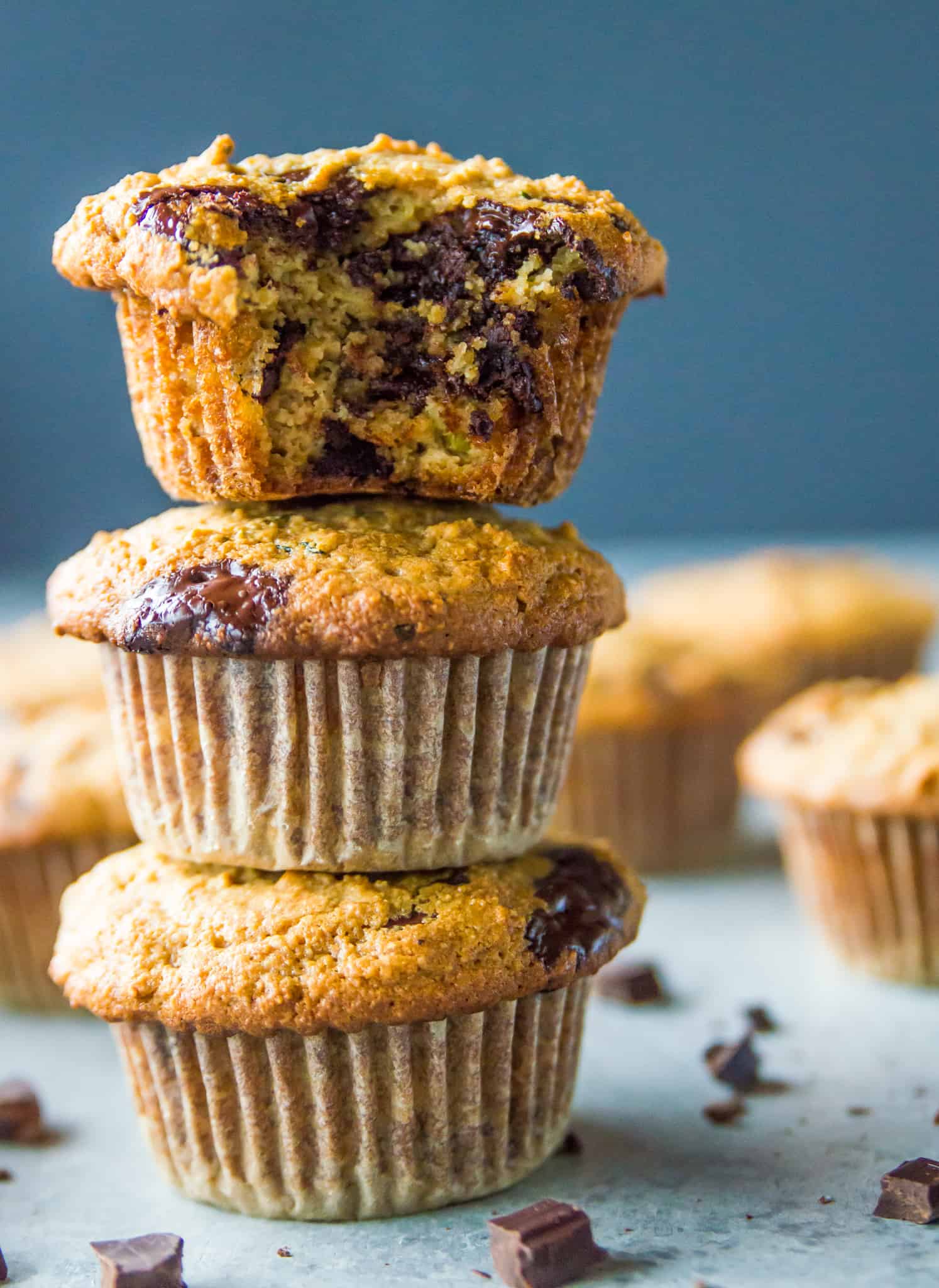 A stack of three zucchini muffins, the top one with a bite out of it showing chunks of chocolate.