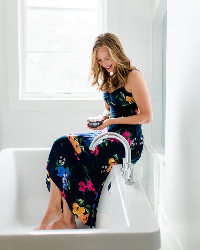A girl in a floral dress sitting on the edge of a tub 