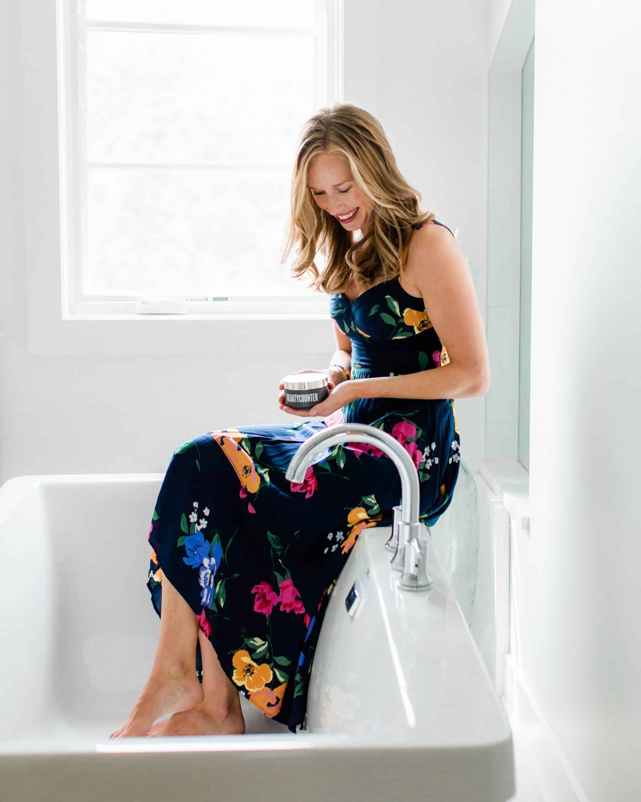 A girl in a floral dress sitting on the edge of a tub. 