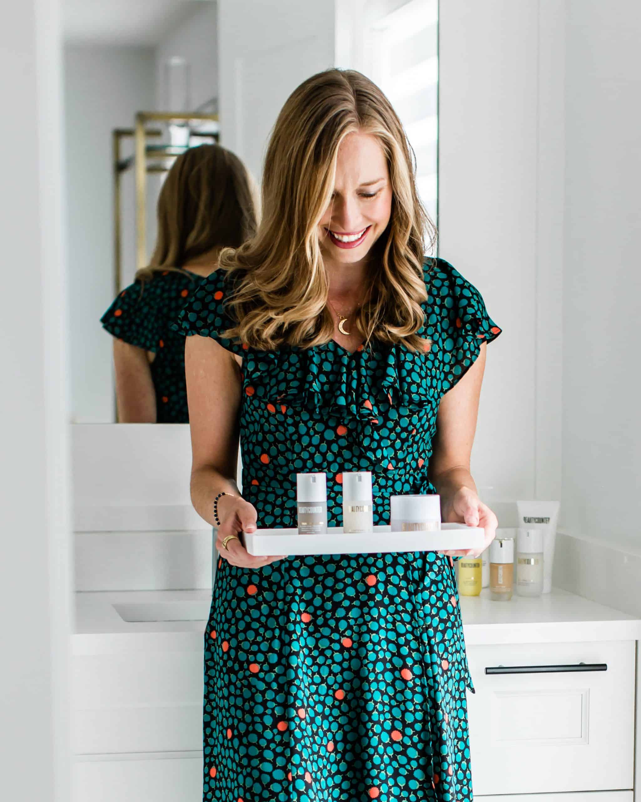 A girl in a floral dress holding Beautycounter products on a tray. 