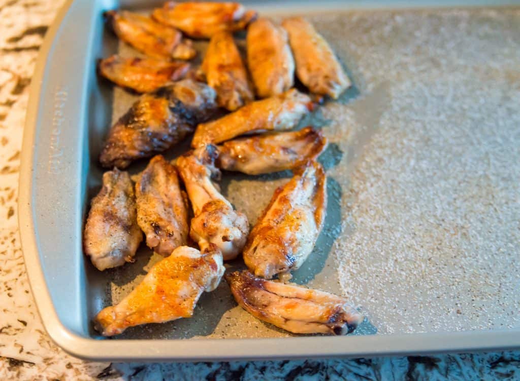 Cooked chicken wings on a baking sheet coated in salt and pepper. 