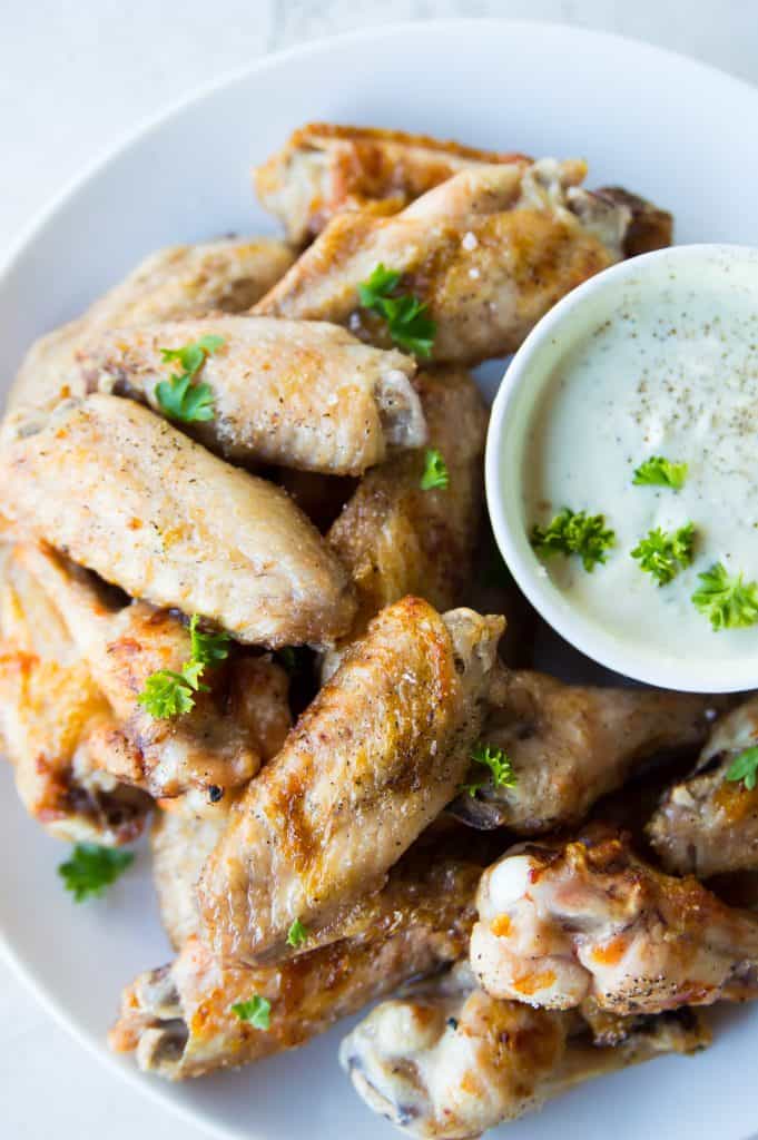 A plate full of chicken wings with a bowl of ranch dip 