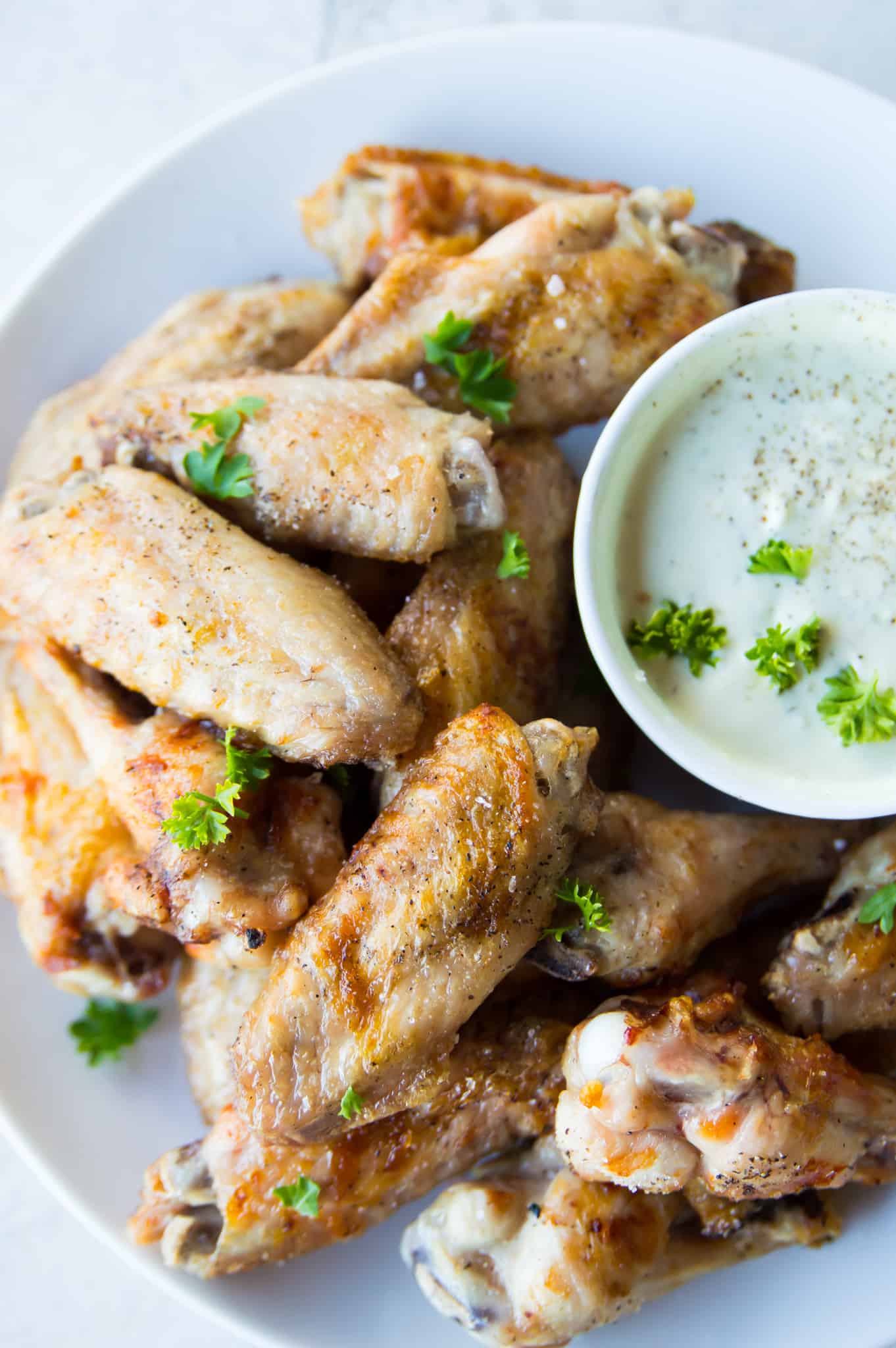 A plate full of cooked salt and pepper chicken wings with a bowl of ranch dip. 