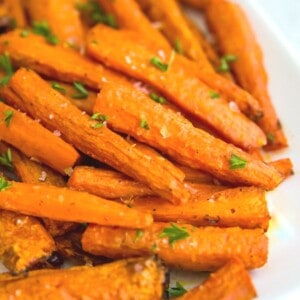 A plate of roasted, sliced carrots with parsley on top for garnish.