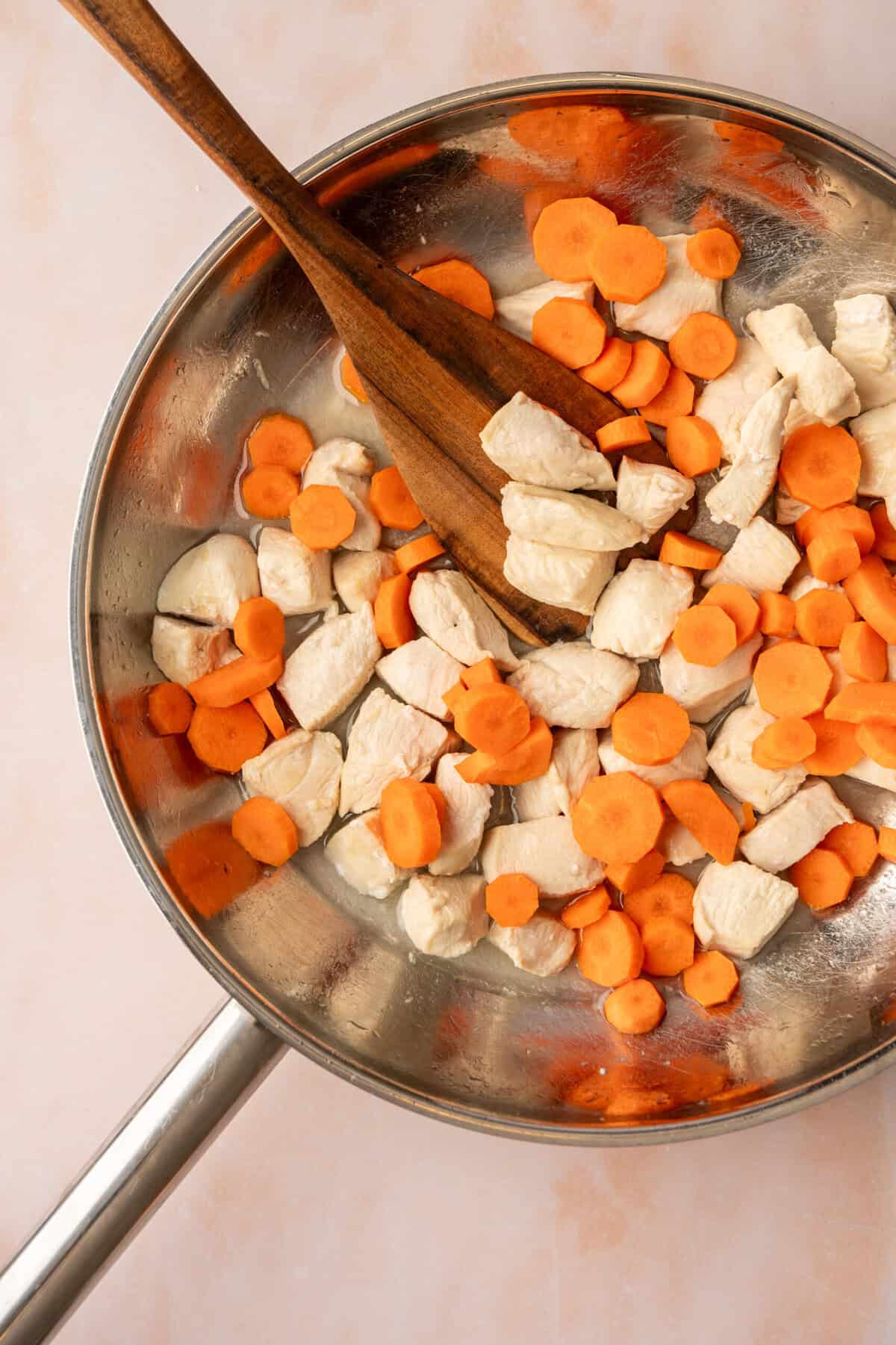 Chopped chicken pieces and carrots cooking in a pan.