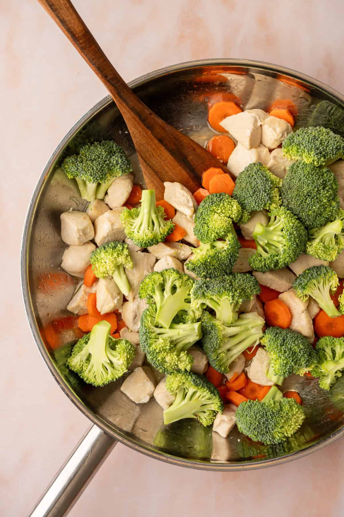 A pan with chopped broccoli, carrots and chicken cooking in it.