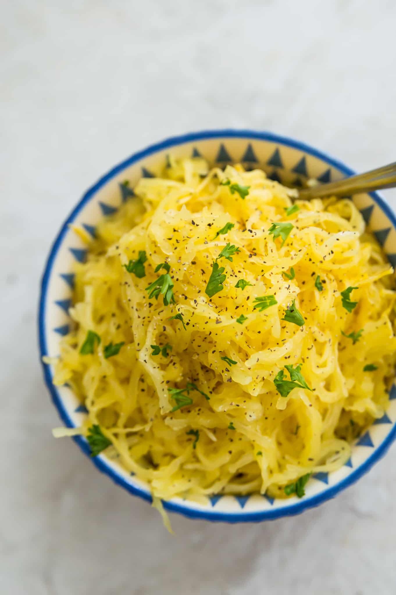 A bowl of cooked spaghetti squash with parsley on top.
