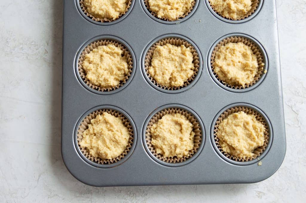 A muffin tray filled with parchment paper muffin cups and the batter to make paleo cornbread muffins.