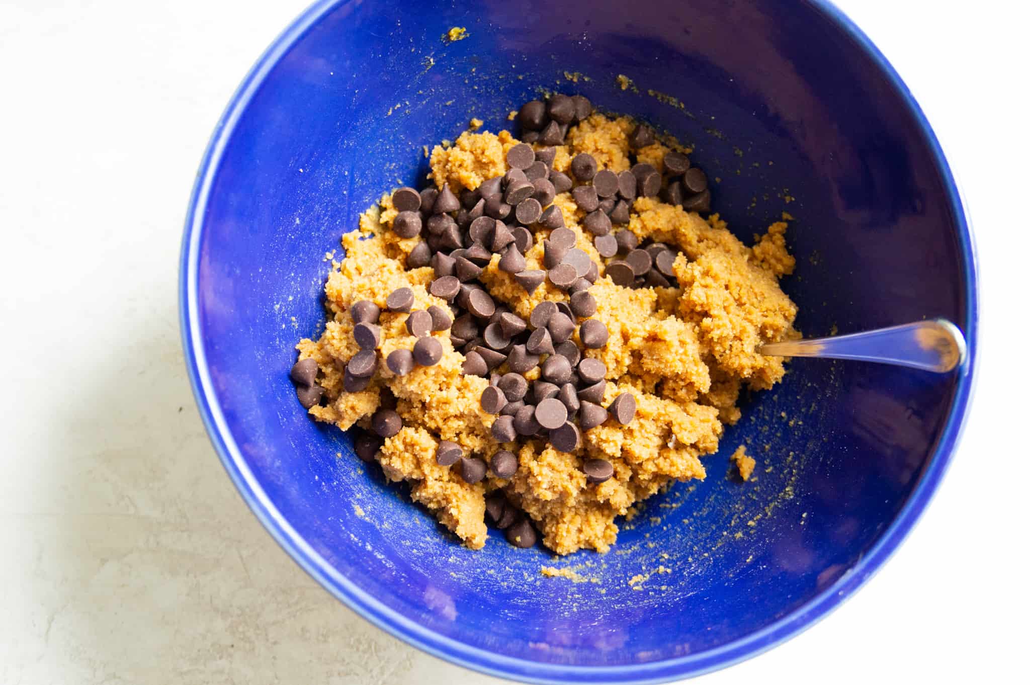 A bowl with chocolate chip cookie dough in it with a spoon in the dough.