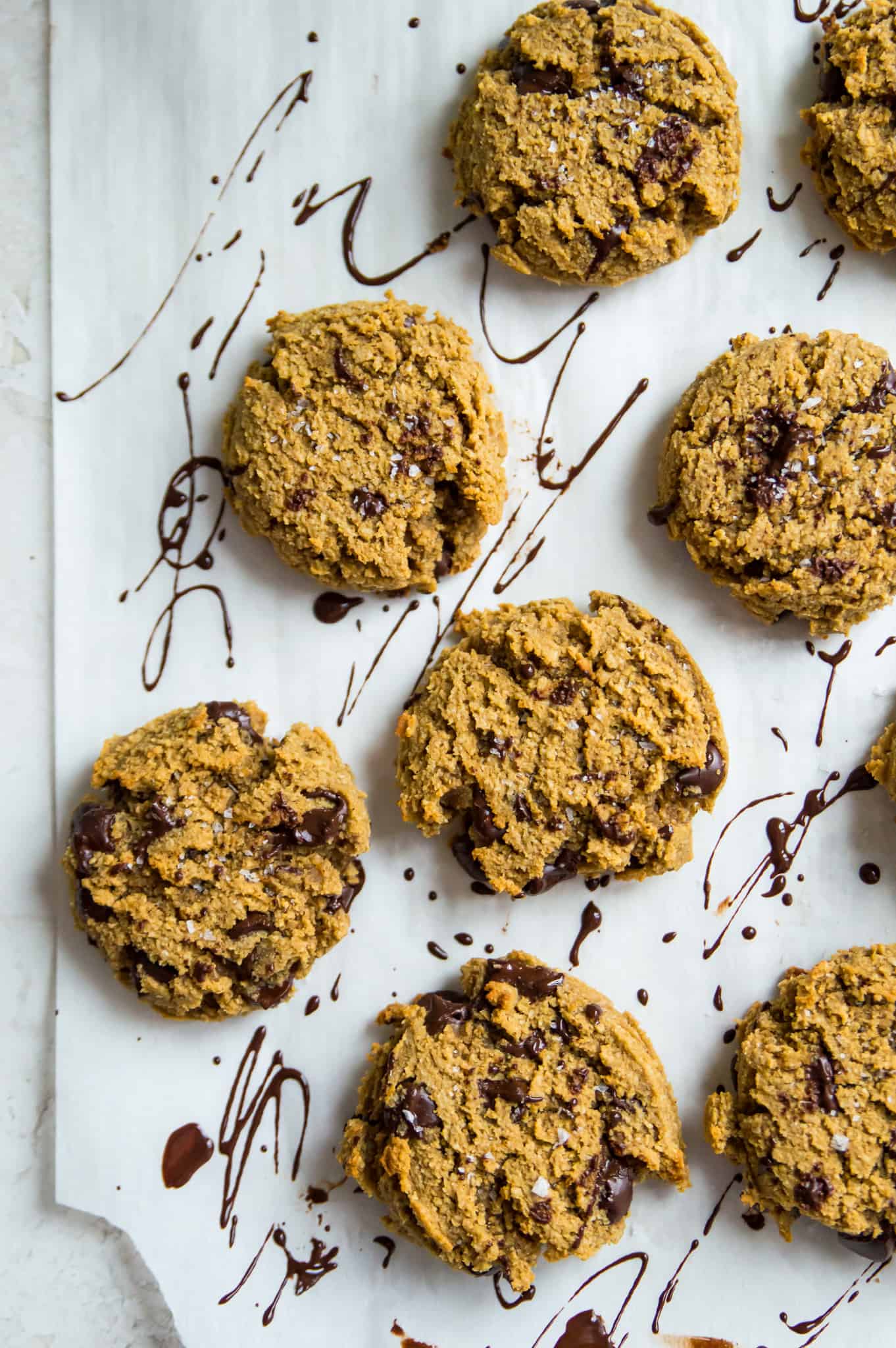 A baking sheet lined with parchment paper with baked chocolate chip cookies on it.