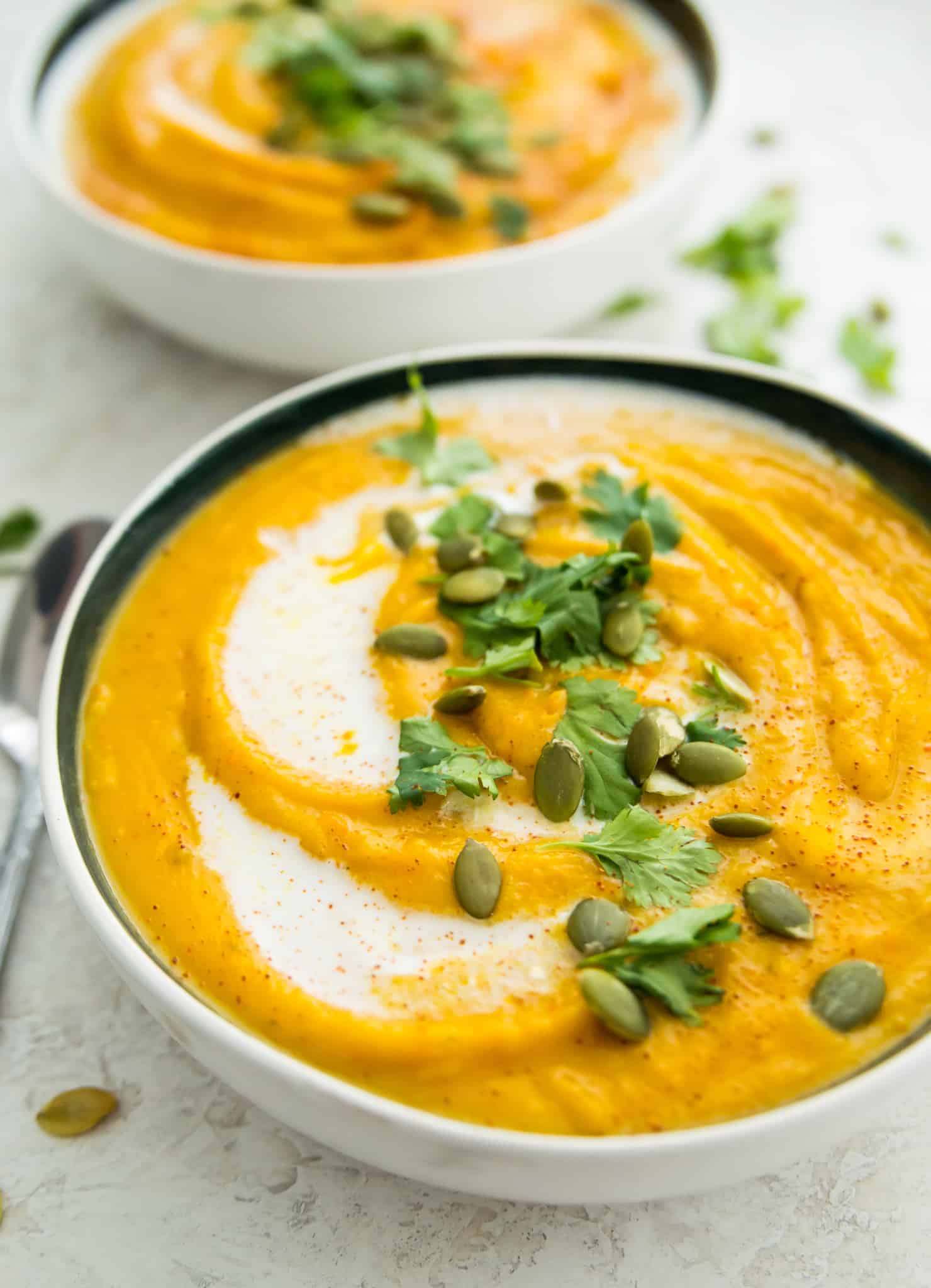 Two bowls of pumpkin and sweet potato soup topped with fresh cilantro and pumpkin seeds. 