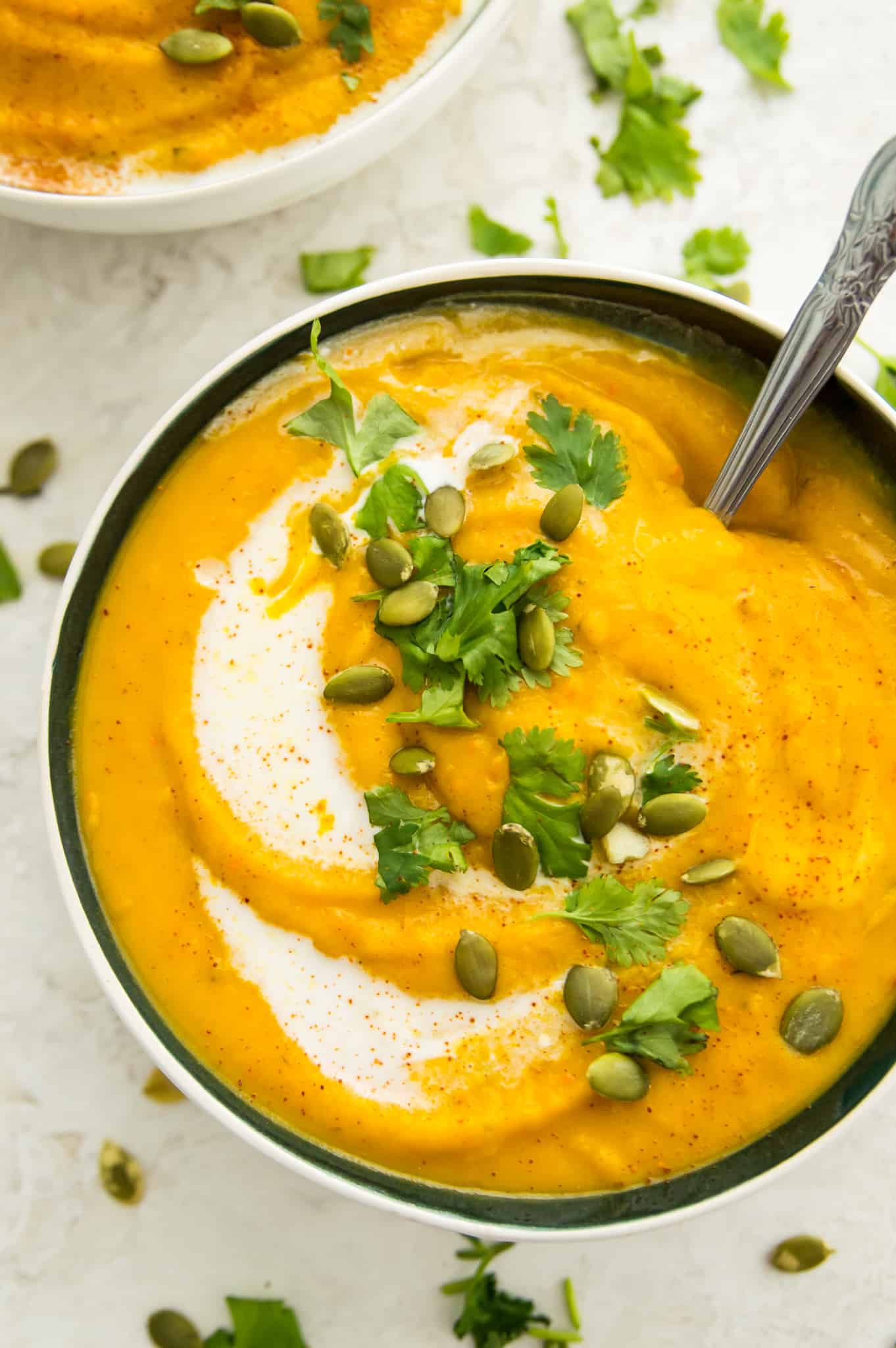 A bowl of pureed Paleo pumpkin and sweet potato soup garnished with pumpkin seeds and herbs.