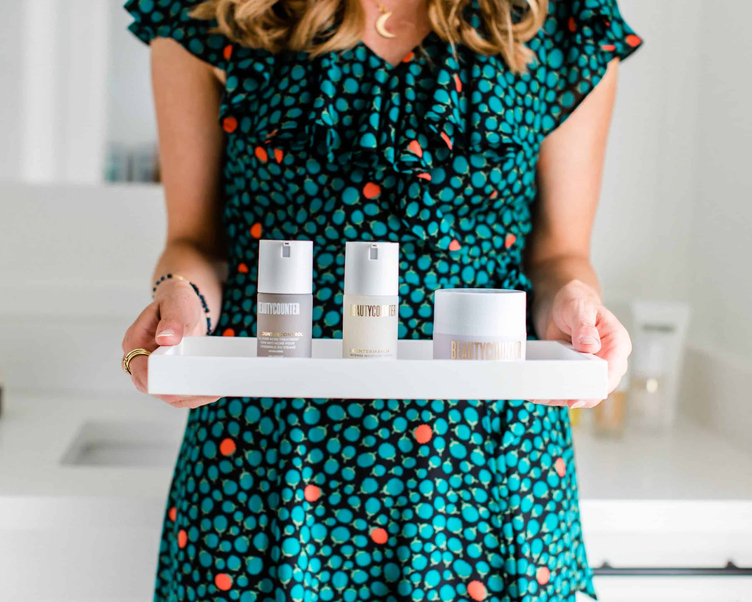 A girl holding a tray filled with three Beautycounter products.