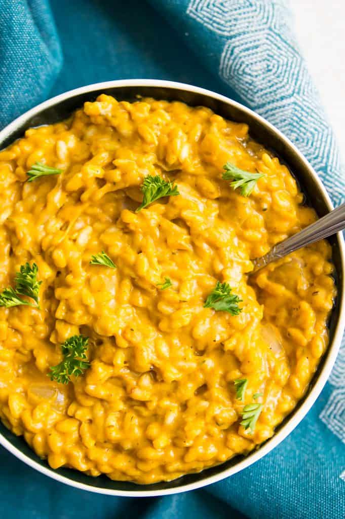 A bowl of vegan pumpkin risotto with a spoon and garnished with parsley