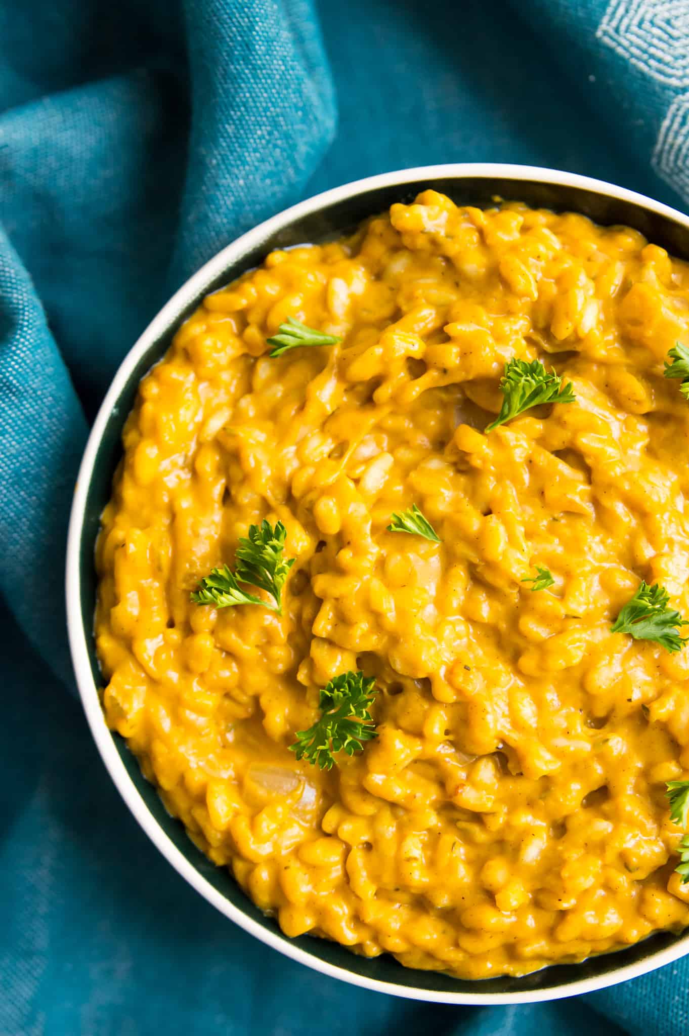 A large bowl of pumpkin risotto garnished with fresh parsley and a blue hand towel beside it.