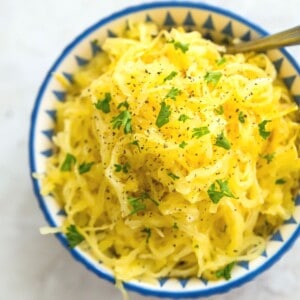 A bowl of cooked spaghetti squash garnished with fresh parsley and black pepper.