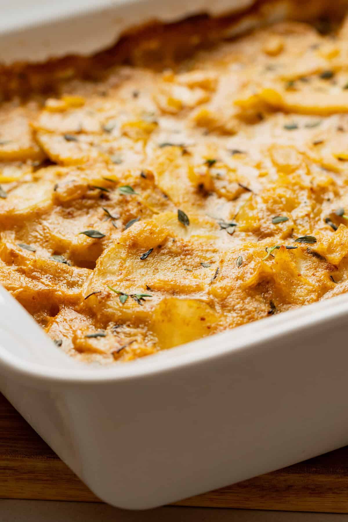 A casserole dish filed with cooked dairy free scalloped potatoes topped with fresh thyme.