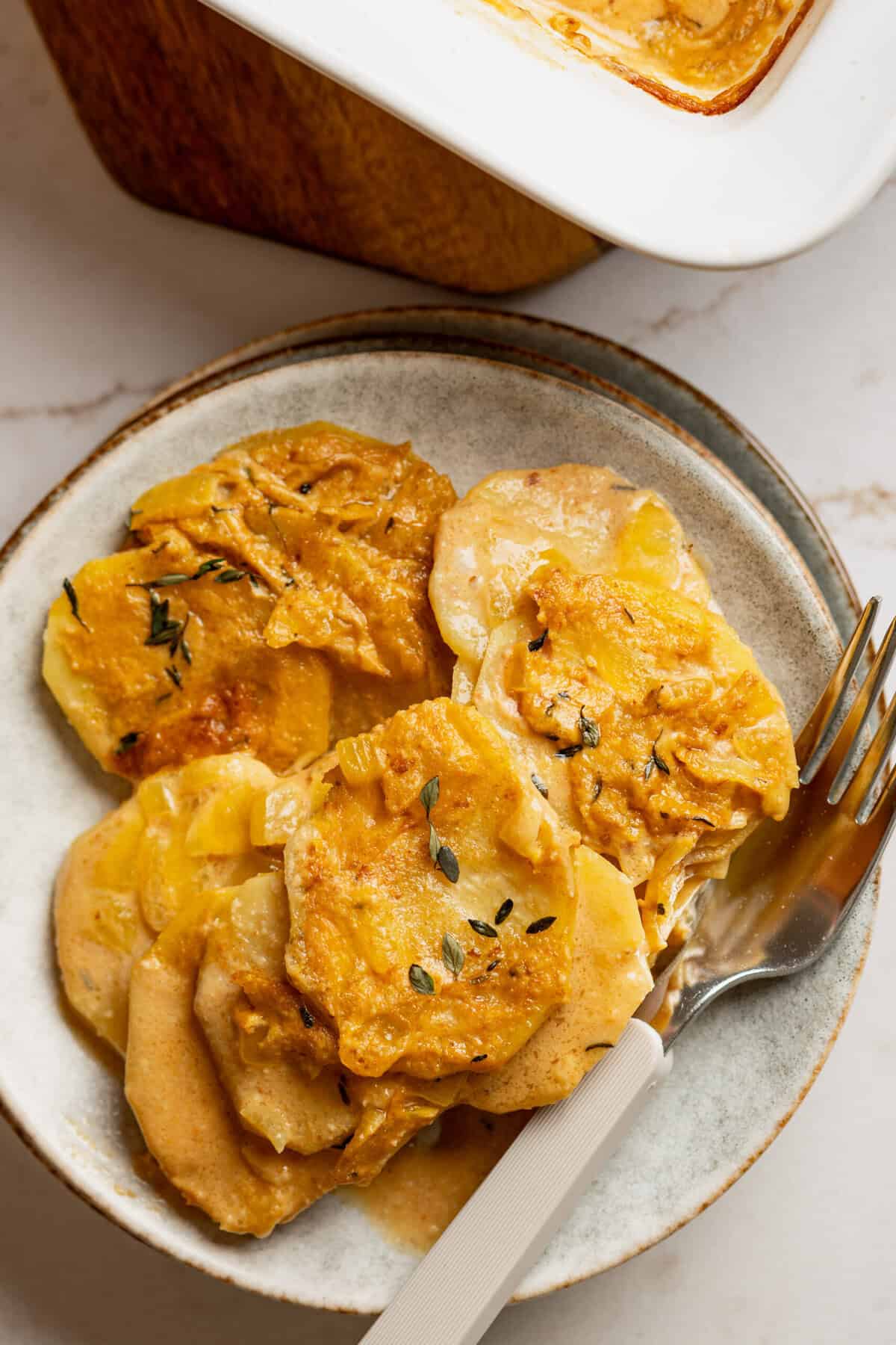 A plate with cooked scalloped potatoes on it and a fork on the plate.