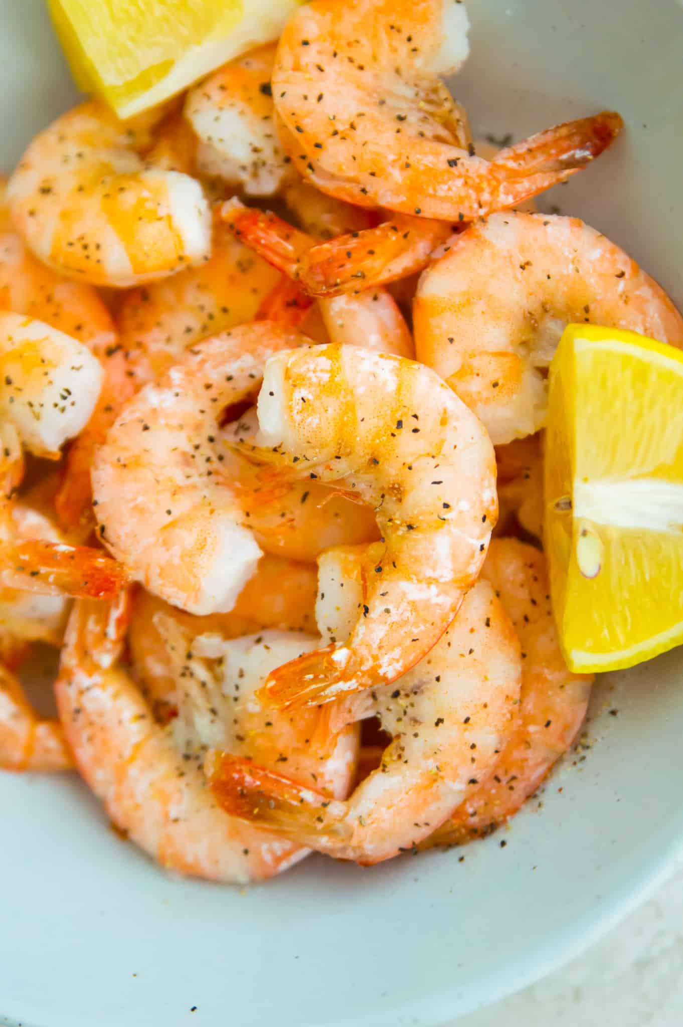A bowl full of cooked shrimp with lemon slices around them. 