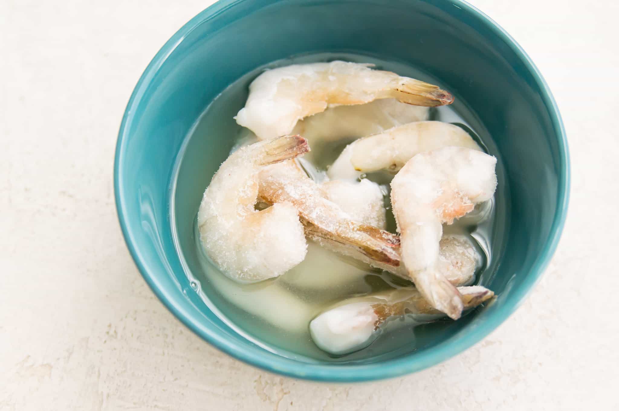 Frozen shrimp being soaked in a bowl of melted butter. 