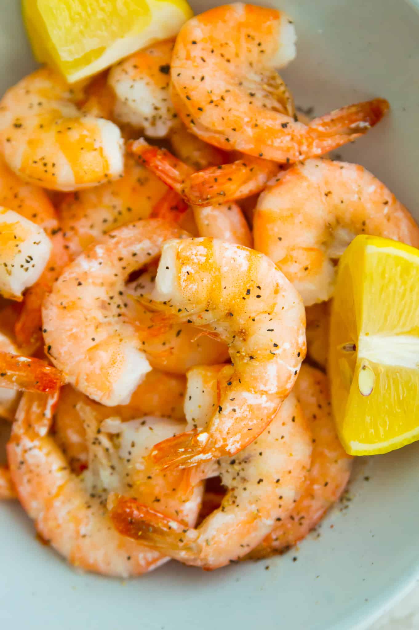 A bowl full of cooked shrimp with slices of lemon around them.