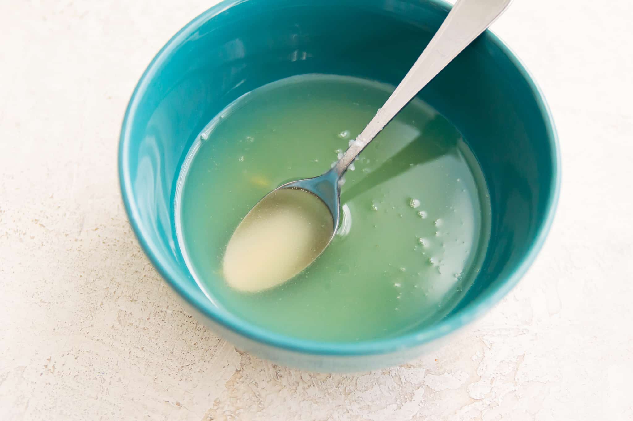 Melted butter and lemon juice together in a blue bowl with a spoon in it.
