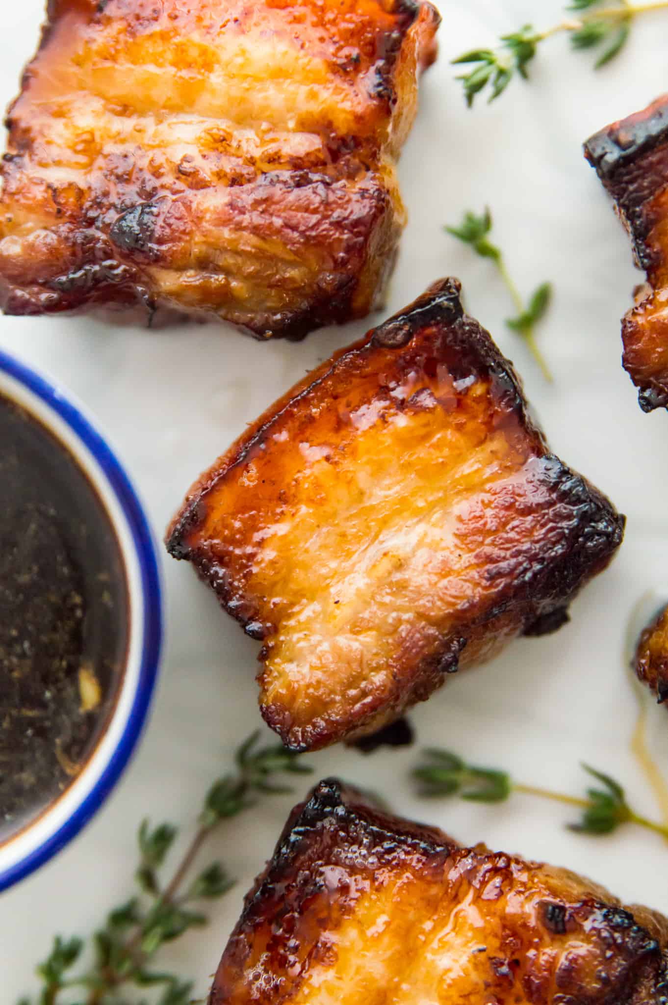 Three pieces of cooked pork belly on a plate with fresh thyme around them.
