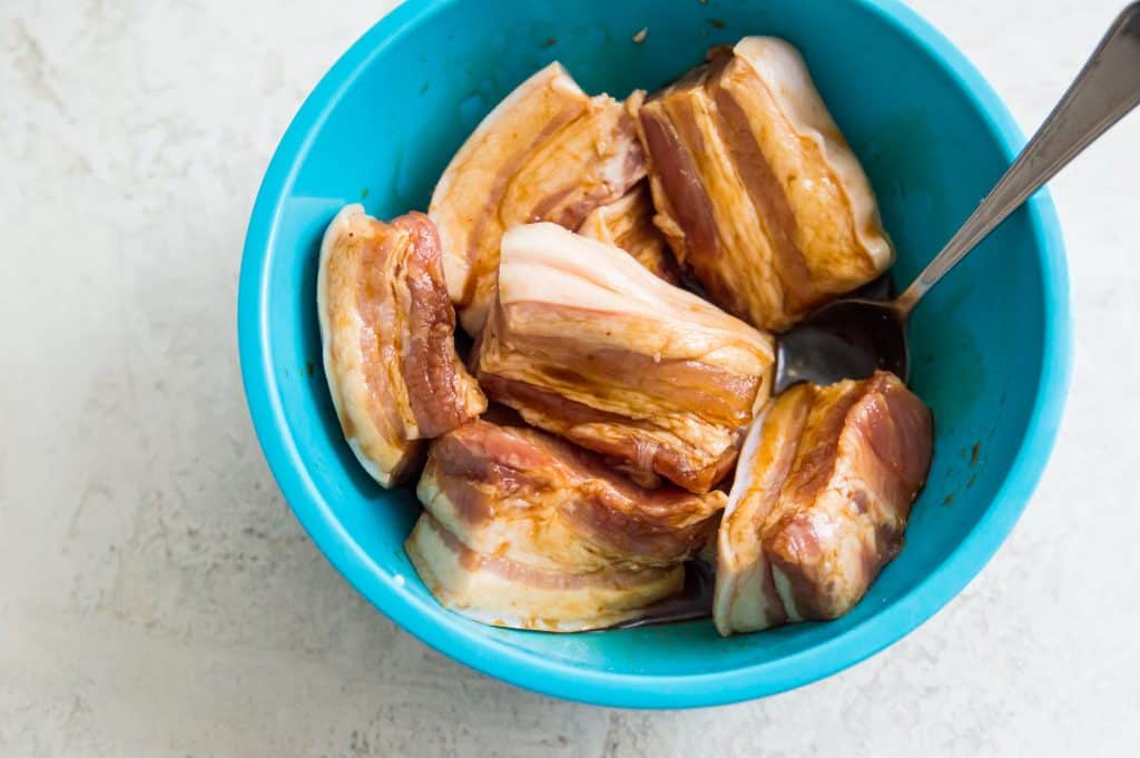 Pork belly pieces being marinaded in a bowl. 