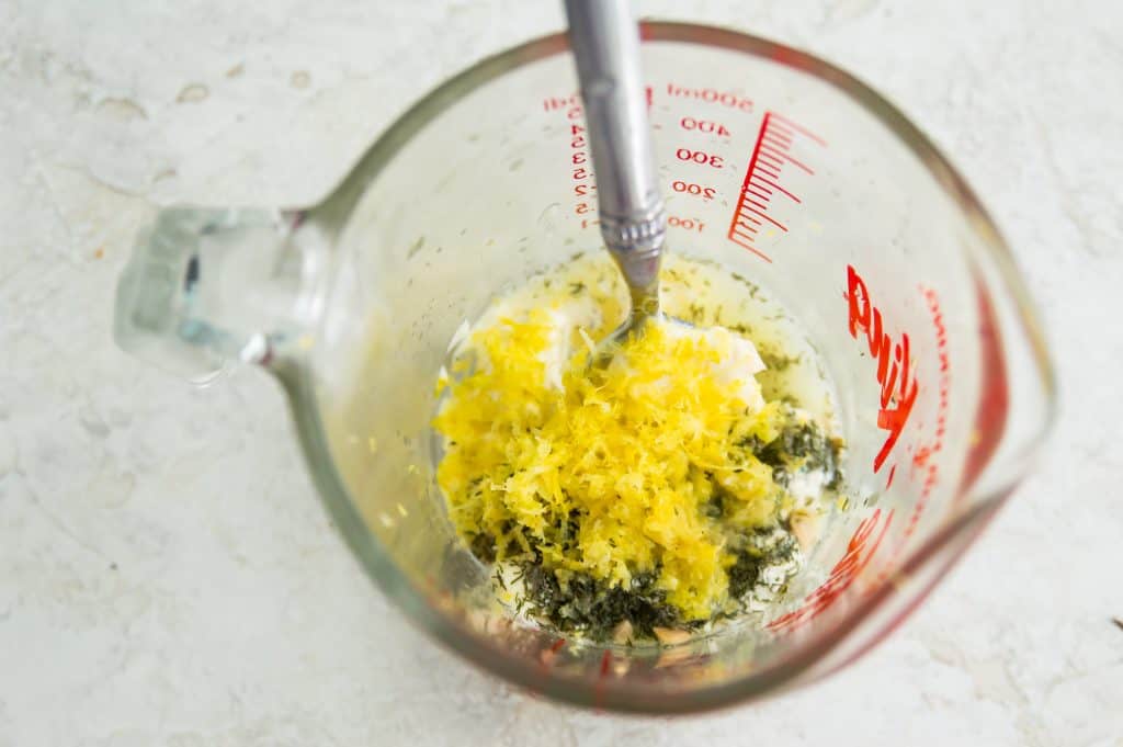 The ingredients for making a lemon dill aioli in a glass measuring cup with a spoon. 
