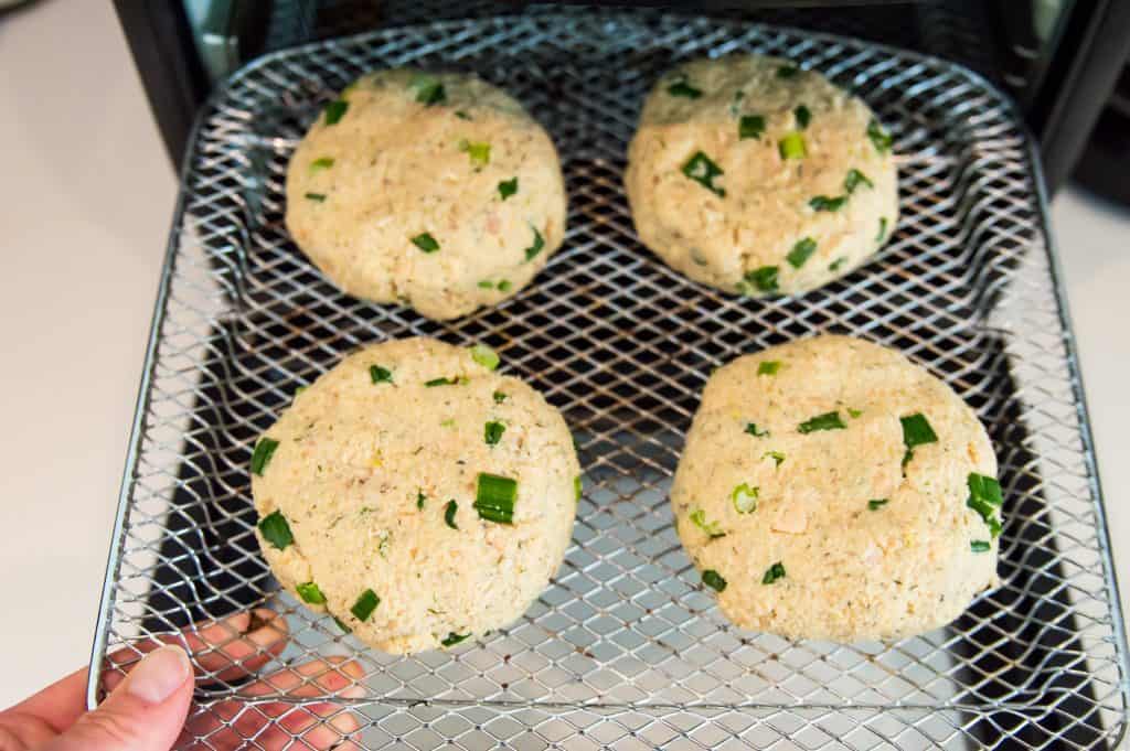Four uncooked salmon patties on an air fryer tray. 